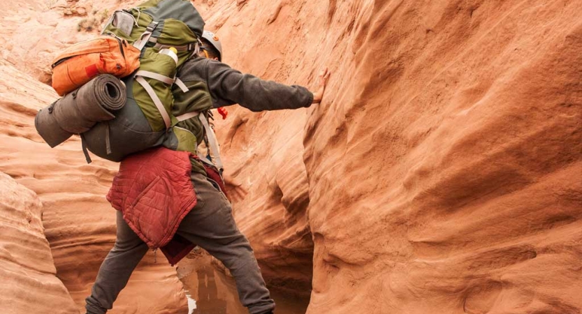 A person carrying a backpack makes their way through a slot canyon